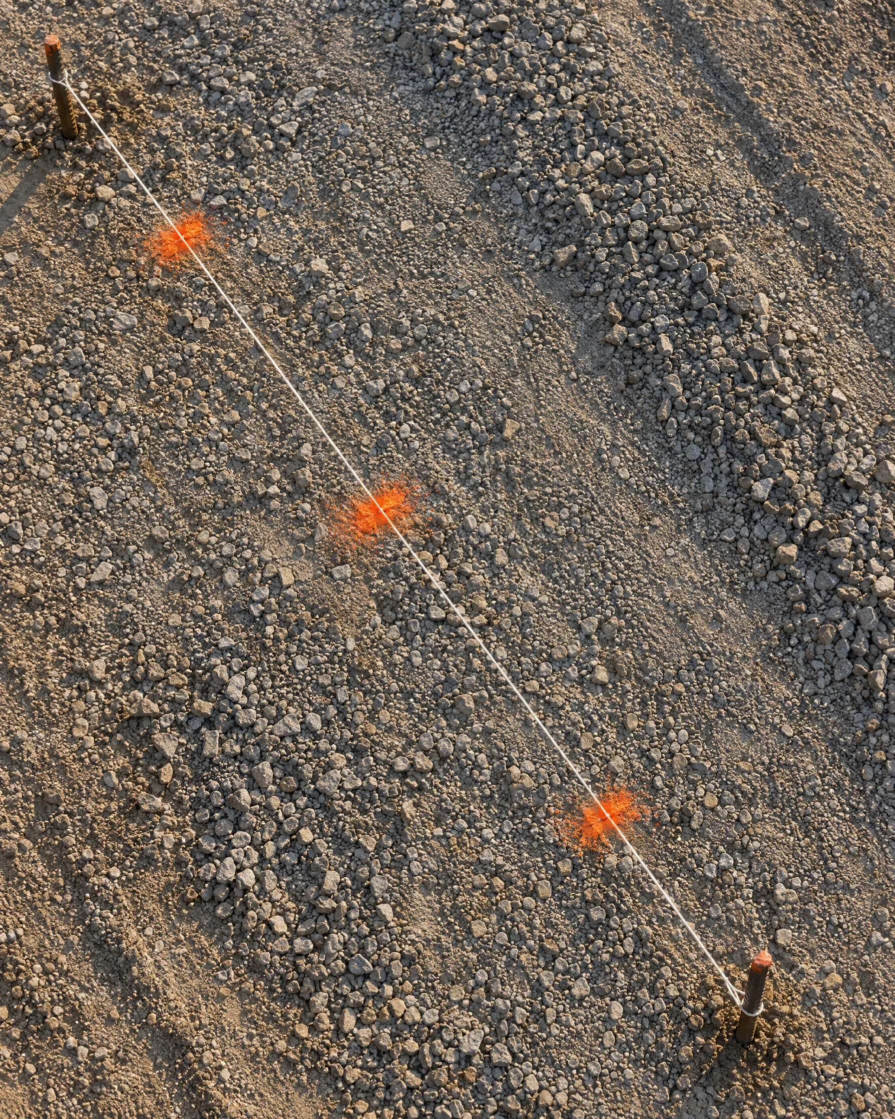 Gespannte Maurerschnur mit orangen Markierungen auf verdichtetem Schotter