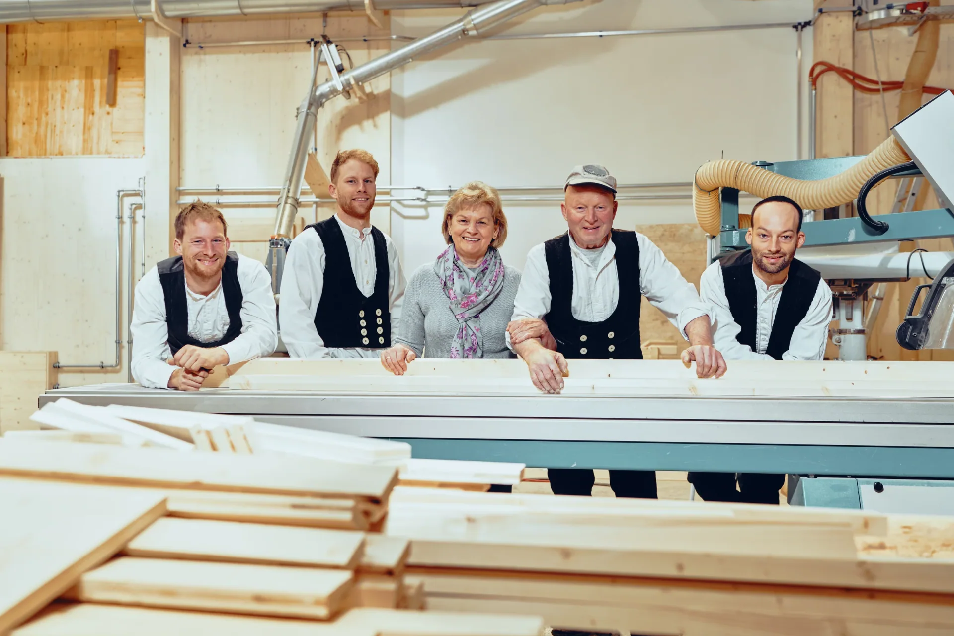 Das Team der Zimmerei Franz Rohrer in Zunftkleidung an einem Arbeitstisch in der Halle