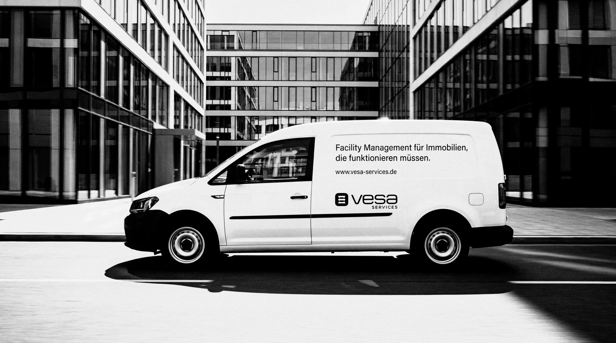 Weißer VW Caddy mit VESA-Beschriftung vor einem Bürogebäude aus Glas